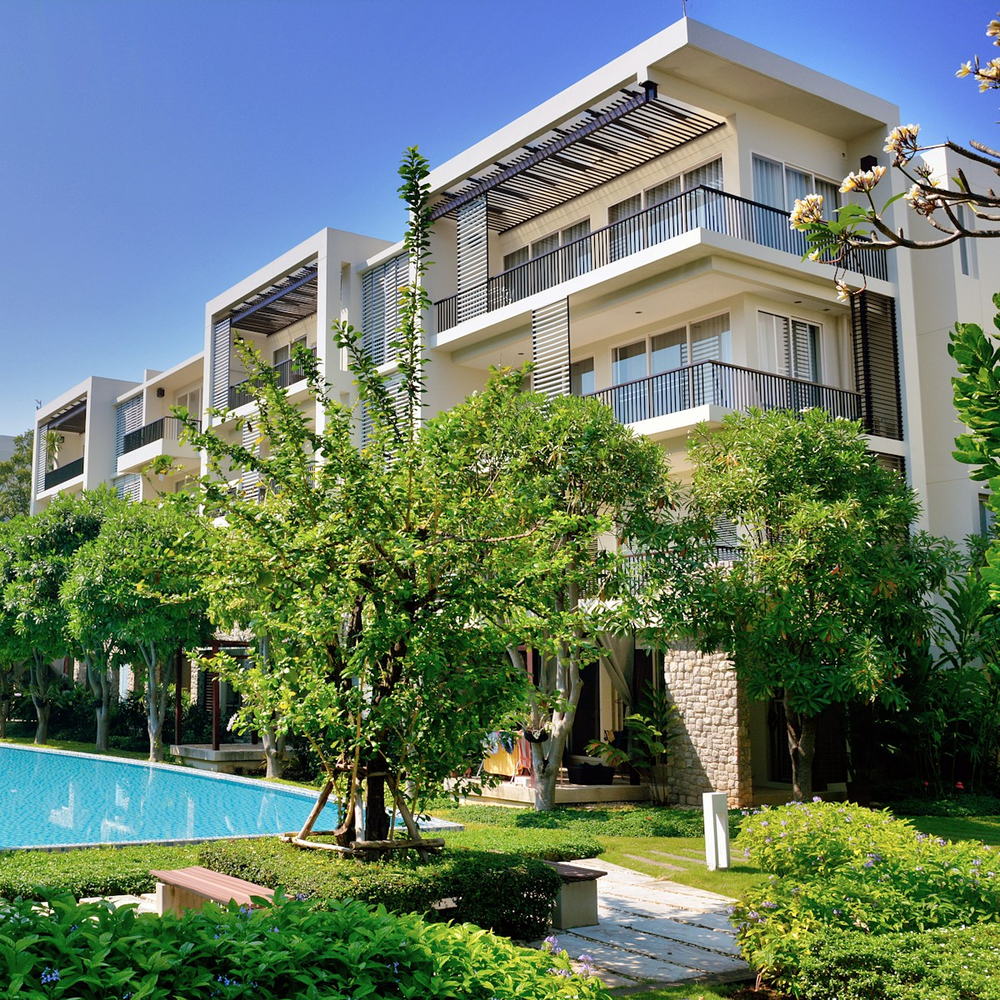 Apartment building with white balconies beside a pool and green trees